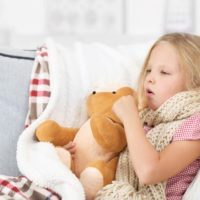 Little girl coughing holding her teddy bear